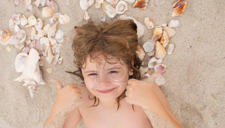 Photo for Child on sea beach. Happy Summer vacation. Cute blonde child relax on sand. Child play with Sea shells and fine beach sand. Kid laying on sandy beach with Shells. Tanned kids face - Royalty Free Image