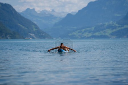 Photo for Muscular man with paddle board. Man paddling on paddleboard. Muscular strong Hispanic man on sup board paddle surfing. SUP surfing in summer vacation in Alps lake in Swiss - Royalty Free Image