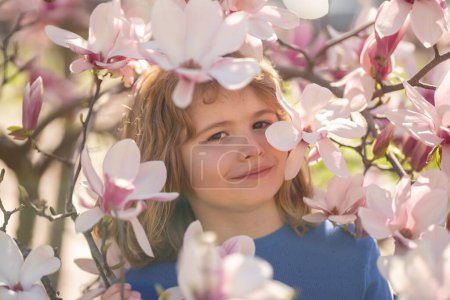 Photo for The spring holidays. Happy kid playing under blooming cherry tree with flowers. Kids face near spring blossom nature background. Spring fun. Kid outdoors in a beautiful spring garden - Royalty Free Image