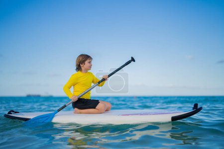 Téléchargez les photos : Kid swimming on stand up paddle board. Water sports, active lifestyle. Kid paddling on a paddleboard in the ocean. Child Paddle boarder. Summer Water sport, SUP surfing. Summer beach vacation - en image libre de droit