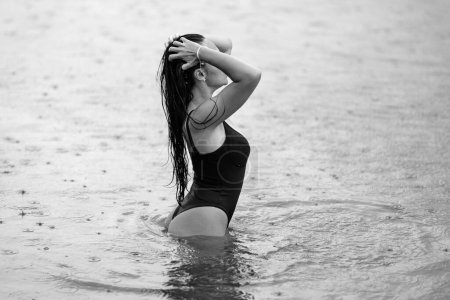 Photo for Summer rain. Woman in bikini Enjoying rainy weather. Summer Bikini Model. Sexy girl on the sea beach. Freedom and carefree concept. Fit sexy woman rest in Summer water in rain - Royalty Free Image