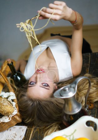 Téléchargez les photos : Jeune femme mangeant de délicieuses pâtes, dégustant des spaghettis maison savoureux à l'intérieur de la cuisine. Pâtes, nouilles, linguine, vermicelles. Cuisine sexy. Femme sexy sur la table de cuisine. Menu de cuisine. Alimentation italienne - en image libre de droit