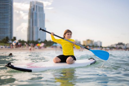 Photo for Kid Paddle boarder. Child boy paddling on paddleboard. Healthy summer lifestyle. Summer Water sport. SUP surfing tour in adventure summer beach vacation. Kid Boy swimming with paddle board - Royalty Free Image