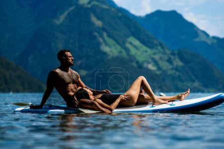 Foto de Sexy pareja de verano. Pareja remando en la naturaleza. Sensual ajuste amantes sexy en tabla de sup paddle surf. Surf SUP en vacaciones de verano. Lago de los Alpes en Suiza. Pareja enamorada en vacaciones de verano en Suiza - Imagen libre de derechos