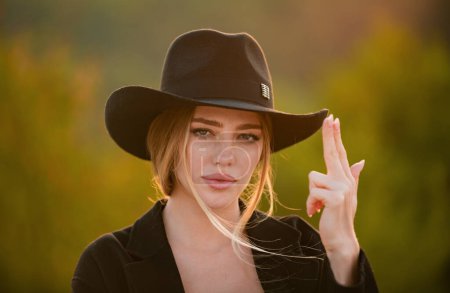 Photo for Beautiful woman in fashion hat. Cowgirl with finger gun. Close up face of young stylish woman simulate shooting with and fingers. Beautiful fashionable girl outdoor portrait - Royalty Free Image