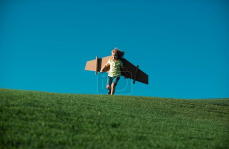 Kind spielt mit Spielzeugflügeln im Park auf grünem Gras-Hintergrund