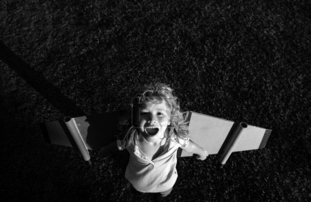 Téléchargez les photos : Voyageur enfant riant avec ailes de sac à dos. Enfant jouant pilote aviateur et rêve à l'extérieur dans le parc - en image libre de droit