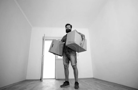 Téléchargez les photos : Man carrying cardboard box on moving day. Delivery man loading cardboard boxes for moving to an apartment - en image libre de droit