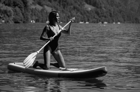 Foto de Hermosa mujer joven que se relaja en el tablero de paddle en el lago de verano o agua de mar. Resort de verano de lujo. Sexy sensual mujer en forma descanso en el agua. Hermosa modelo disfrutando de vacaciones de verano - Imagen libre de derechos