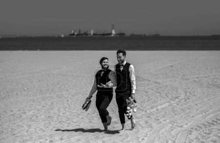 Foto de Hombres gay caminando en una playa. Lgbt matrimonio gay pareja tener romántico momento juntos después de la ceremonia de boda. Concepto de LGBTQ. Boda de pareja gay. Matrimonio gay - Imagen libre de derechos