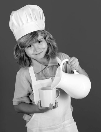 Téléchargez les photos : Du lait pour les enfants. Chef cuisinier enfant prépare la nourriture dans fond bleu studio isolé. Des enfants cuisinent. Jeune garçon avec tablier et chapeau de chef préparant un repas de légumes sains dans la cuisine - en image libre de droit
