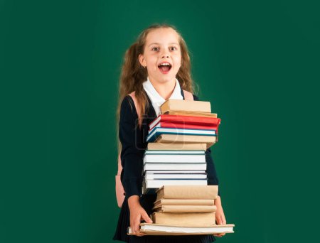 Photo for Knowledge day, Smiling funny little schoolkid girl with backpack hold books on green blackboard. Childhood lifestyle concept. Education in school - Royalty Free Image