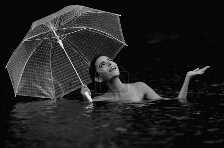 Sexy topless Woman with umbrella in water. Summer rain. Rainy weather. Rain rain go away. Sexy woman sensually relaxing in water. Recreation wellness and wellbeing. Sensual rain