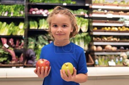 Téléchargez les photos : Enfant avec des pommes à l'épicerie. Petit enfant choisissant de la nourriture dans une épicerie ou un supermarché - en image libre de droit