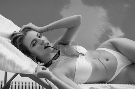 Téléchargez les photos : Femme de mode dans la piscine de luxe. Femme sexy élégante dans le bikini blanc sur le corps mince bronzé posant près de la piscine. Riche repos d'été - en image libre de droit