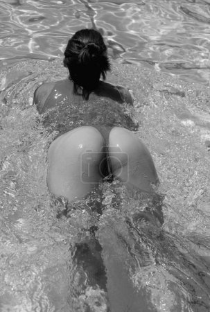 Téléchargez les photos : Summer butt in water. Close-up beautiful slim back of a beautiful woman in a swimsuit posing in the swimming pool water. Sexy tanned body, perfect figure. Rest on a tropical. Sexy buttocks - en image libre de droit