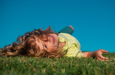 Photo for Kid boy laying on the green grass. Happy child playing in green spring field against sky background. Freedom kids and imagination concept - Royalty Free Image