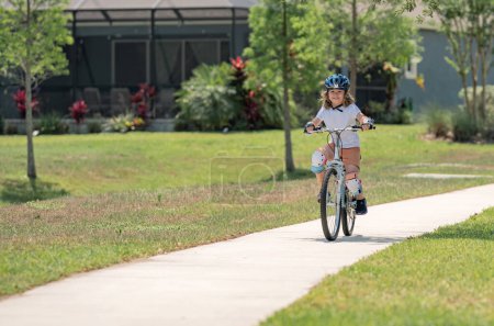 Lindo niño montando una bicicleta en el parque de verano. Los niños aprenden a conducir una bicicleta en un camino de entrada afuera. Niño montar en bicicleta en la ciudad con cascos como equipo de protección. Niño en bicicleta, bicicleta al aire libre