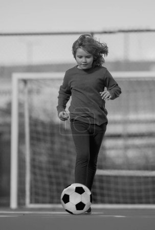 Child boy football or soccer player in action on stadium kicking football ball for goal. Concept of sport, competition. Kid play football ball. Kid with football ball. Sport, soccer hobby for kids