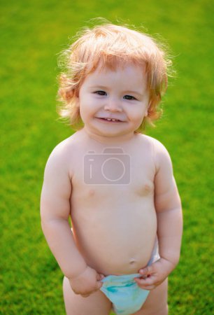 Foto de Retrato de un niño pequeño en pañal jugando al aire libre en la hierba. Bebé y verano tiempo soleado. Gracioso retrato de primer plano de niño. Niño rubio, emoción sonriente, cara sonriente feliz - Imagen libre de derechos