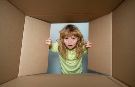 Photo for Funny child boy is opening gift and looking inside cardboard box. Children expression surprised face - Royalty Free Image