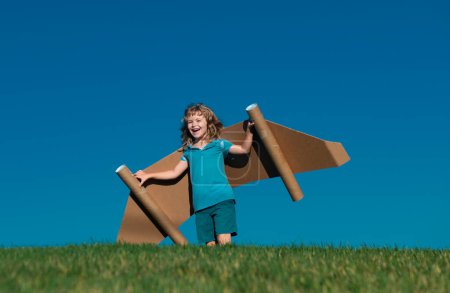 Photo for Kid with toy jetpack outdoor. Child playing in green spring field with cardboard wings. Spring travel and adventure - Royalty Free Image