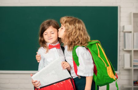 Téléchargez les photos : Amis d'école, câlins et baisers. Portrait de deux élèves heureux qui étudient en classe à l'école primaire - en image libre de droit