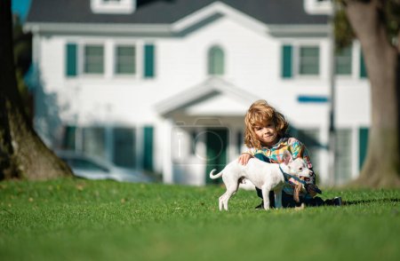 Téléchargez les photos : Enfant embrasse avec amour son chien de compagnie. Joyeux petit garçon jouant avec chiot dans le jardin - en image libre de droit