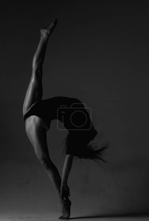 Photo for Leg-split. Sexy ballerina in black underwear stretching on black background. Concept of ballet art. Sexy pole dancer. Beautiful sexy fitness girl with great figure flexing her perfect body - Royalty Free Image