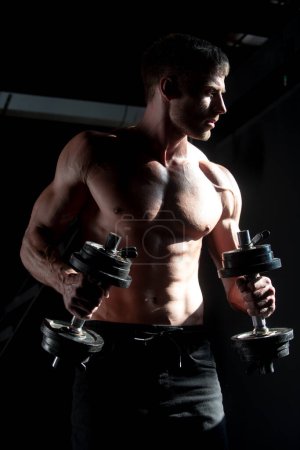 Photo for Muscular man working out in gym doing exercises with dumbbell. Muscular sexy man doing exercises with dumbbell. Sporty man working out on black. Muscular naked torso - Royalty Free Image