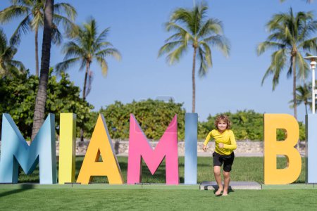 Photo for Kid near Miami Beach sign. Kid enjoy summer vacation holiday. Travel, childhood happiness concept. Summer Holiday at Miami Beach Florida. Blond little kid boy having fun on Miami beach, Ocean drive - Royalty Free Image