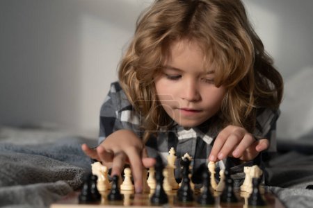 Téléchargez les photos : Le petit garçon joue aux échecs à la maison. L'enfant pense au jeu d'échecs. Étudiant intelligent, intelligent et intelligent. Jeux pour le concept intelligence cérébrale - en image libre de droit