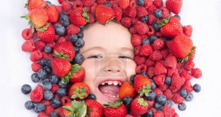Téléchargez les photos : Vitamines saines fruits. Visage enfant aux baies mélange de fraises, bleuets, framboises, mûres - en image libre de droit