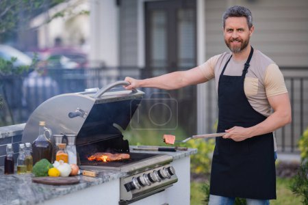 Photo for Male chef grilling and barbequing in garden. Barbecue outdoor garden party. Handsome man preparing barbecue meat. Concept of eating and cooking outdoor during summer time - Royalty Free Image