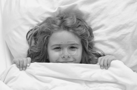 Photo for Kid under covers, face cover with blanket. Cute awaking child in bed, bedtime, childhood and growth kids concept, close-up indoor portrait - Royalty Free Image