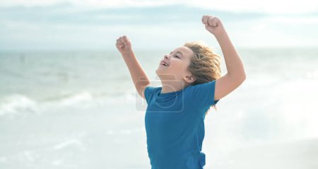 Téléchargez les photos : Enfant excité. Visage émotionnel expressif. Enfant mignon jouant en plein air sur la plage d'été. Petit enfant en vacances d'été. Concept vacances d'été. Bonne enfance - en image libre de droit