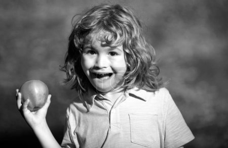 Foto de Retrato de niño sosteniendo y comiendo una manzana sobre fondo verde de la naturaleza - Imagen libre de derechos