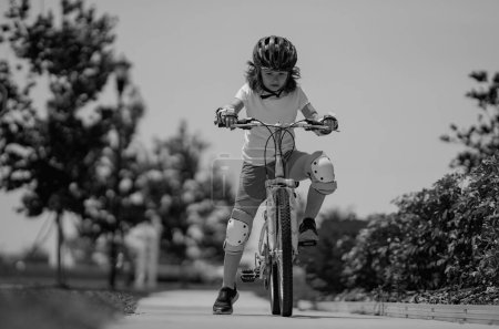 Petit enfant en vélo dans un parc d'été. Les enfants apprennent à conduire un vélo sur une allée à l'extérieur. Enfant à vélo dans la ville portant des casques comme équipement de protection. Enfant à vélo extérieur