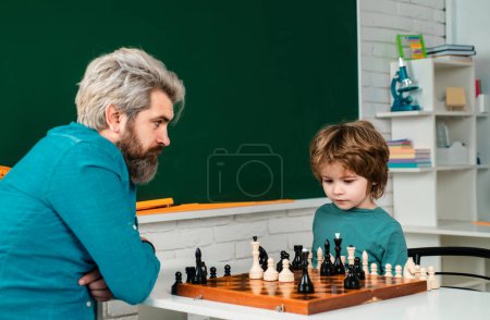 Home tutor helping boy with studies chess. Happy little kid playing chess with senior man at home