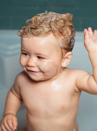 Téléchargez les photos : Bain moussant pour enfants. Bains de bébé heureux drôles dans la baignoire avec de l'eau et de la mousse. Hygiène des enfants - en image libre de droit