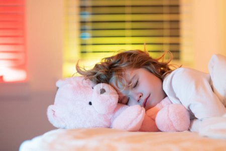 Guten Schlaf. Schönes Gesicht eines blonden kaukasischen Kindes, das mit einem Spielzeug-Teddybär auf dem Bett schläft. Süße Träume. Kleiner Junge schläft zu Hause im Bett