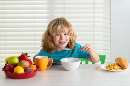 Téléchargez les photos : Un écolier prend son petit déjeuner avant l'école. Portrait de l'enfant assis au bureau à la maison cuisine ont délicieux délicieux petit déjeuner nutritif - en image libre de droit