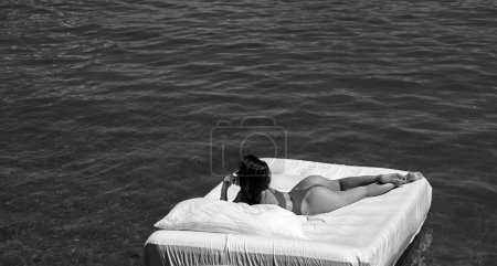 Téléchargez les photos : Confort concept de lit confortable. Femme avec matelas gonflable dans l'eau d'été. Femme sexy dormant ou se reposant sur un matelas dans l'eau. Concept de matelas d'eau. Fais de beaux rêves. Repos d'été - en image libre de droit