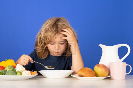 Photo for Sad tired kid boy have a dinner. Child eating soup. Young boy with spoon eating soup. Cute healthy hungry child boy eating soup from bowl with spoon on blue studio background - Royalty Free Image