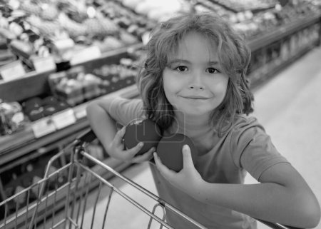Foto de Niño con cesta de la compra con supermercado. Un chico comprando comestibles en el supermercado. Un chico en la tienda. Concepto de compras en el supermercado. Comprando con el carrito de la compra. Tienda de comestibles, cesta de la compra - Imagen libre de derechos