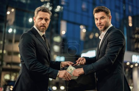 Photo for Investor in suits giving dollar banknotes. Businessman giving money to his partner outdoor. Businessman giving money. Business partnership. Rich business man with money. Giving money concept - Royalty Free Image