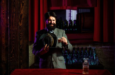 Foto de Feliz hombre barbudo con un vaso de brandy o whisky. hipster barbudo en el bar - Imagen libre de derechos