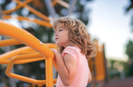 Téléchargez les photos : Cute child boy plays on playground. Kid climbing on playground - en image libre de droit