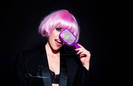 Young funny fashion woman with pink wig, hairdresser with comb brushing hair. Brunette woman combing hair