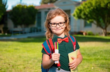 Foto de Un pequeño estudiante sonriente con un libro de mochilas. Retrato de alumno escolar feliz al aire libre - Imagen libre de derechos